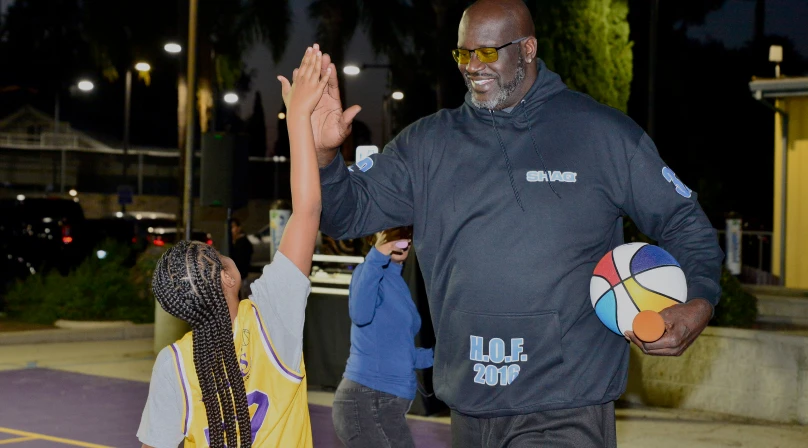 Shaquille O'Neil and a young girl doing a high-five on the Los Angeles Comebaq Court.